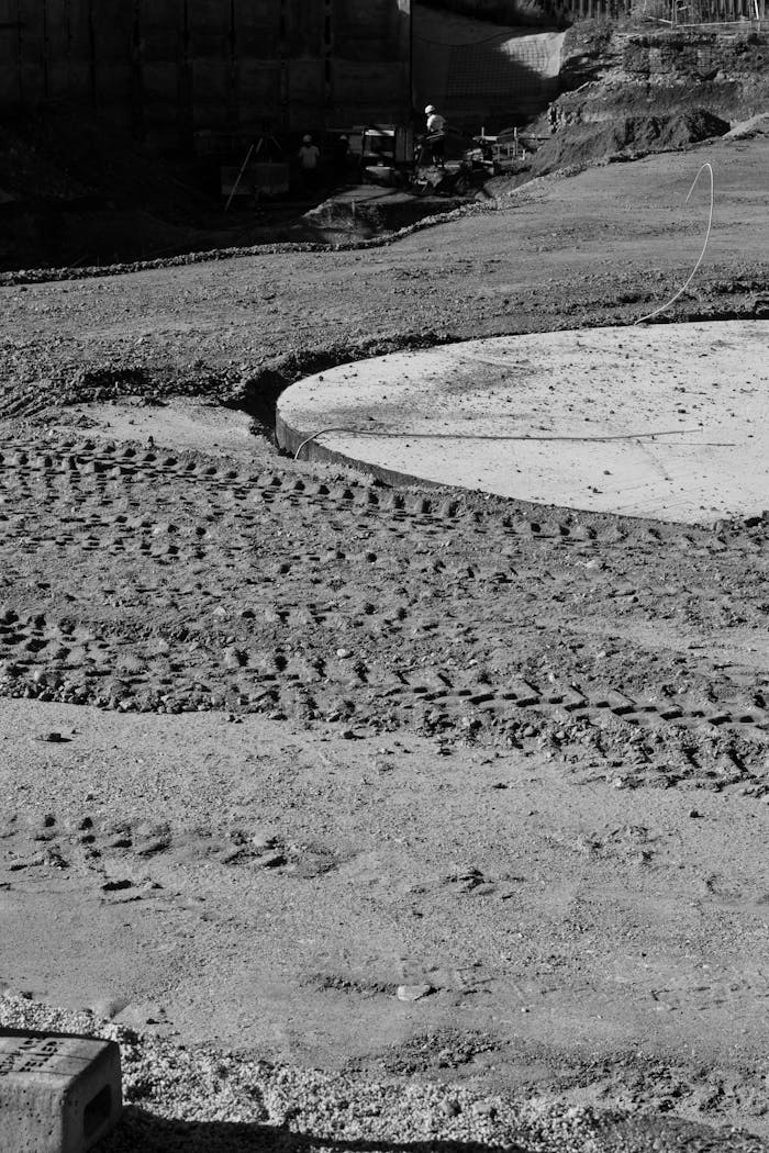 Monochrome image of a construction site with visible tire tracks and concrete circles.